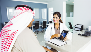 Paciente hispano de mediana edad en consulta médica moderna, escuchando atentamente a una doctora hispana que le explica el diagnóstico de la enfermedad de Fabry usando una tableta digital. La interacción destaca la comunicación en el diagnóstico de Fabry, diferenciando de procesos neurológicos como la esclerosis múltiple.